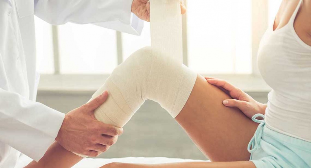 Травматолог на приеме накладывает эластичный бинт