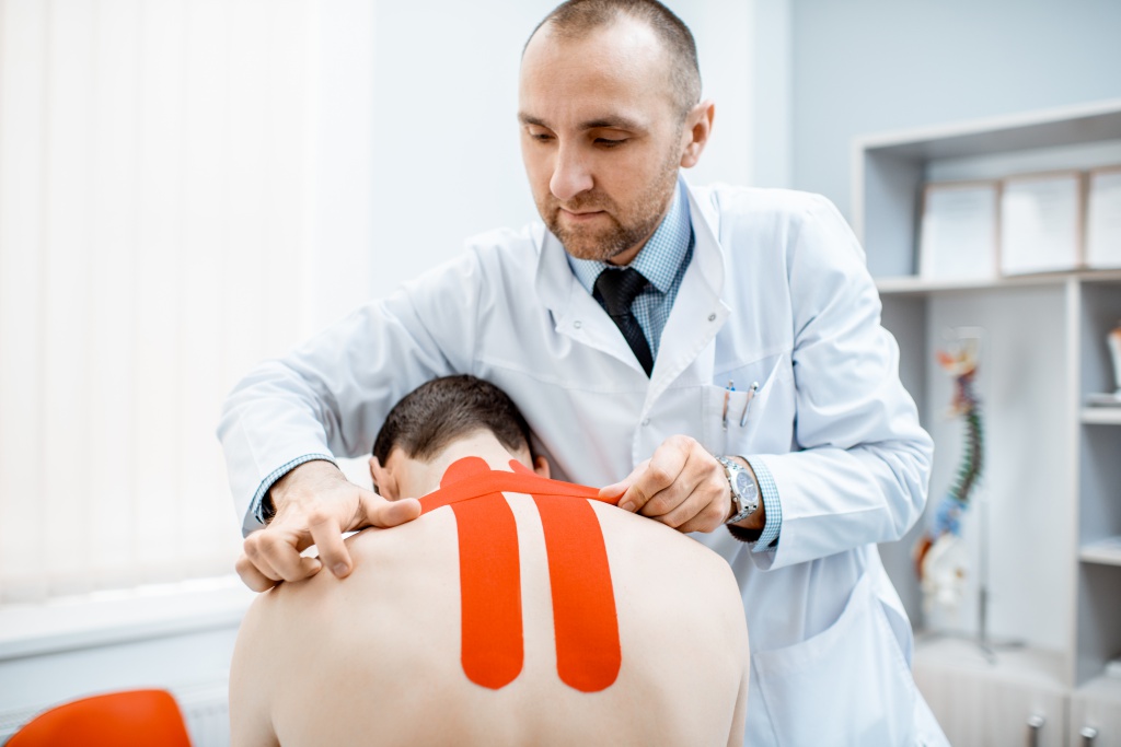 терапевт накладывает кинезио-ленту на мужчину