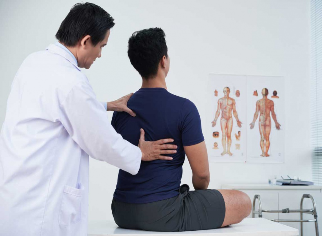 Врач лечит и осматривает пациента со сколиозом